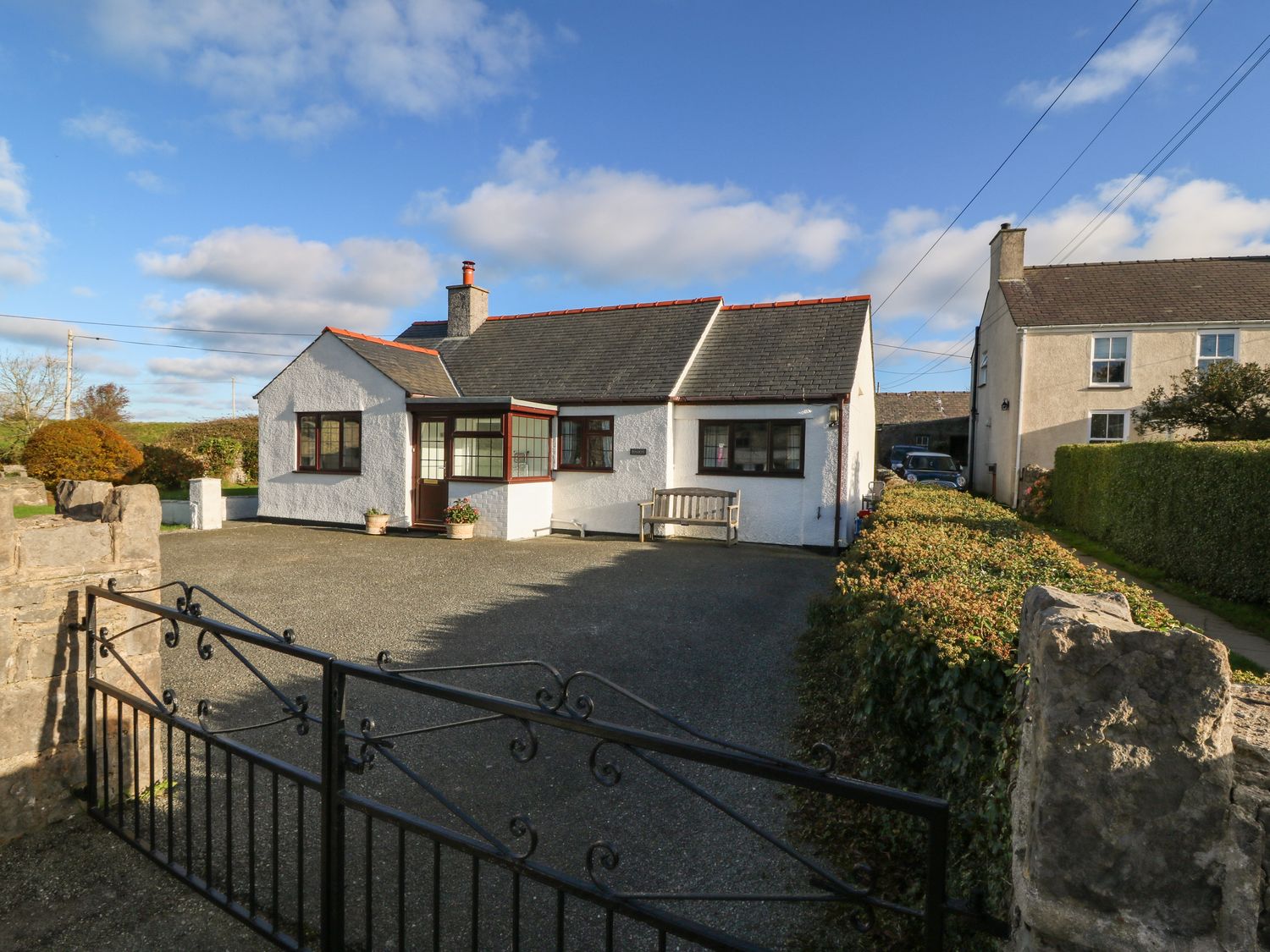 A white detached house with a black iron gate and a driveway at Penllwyn in Llanddona near Beaumaris