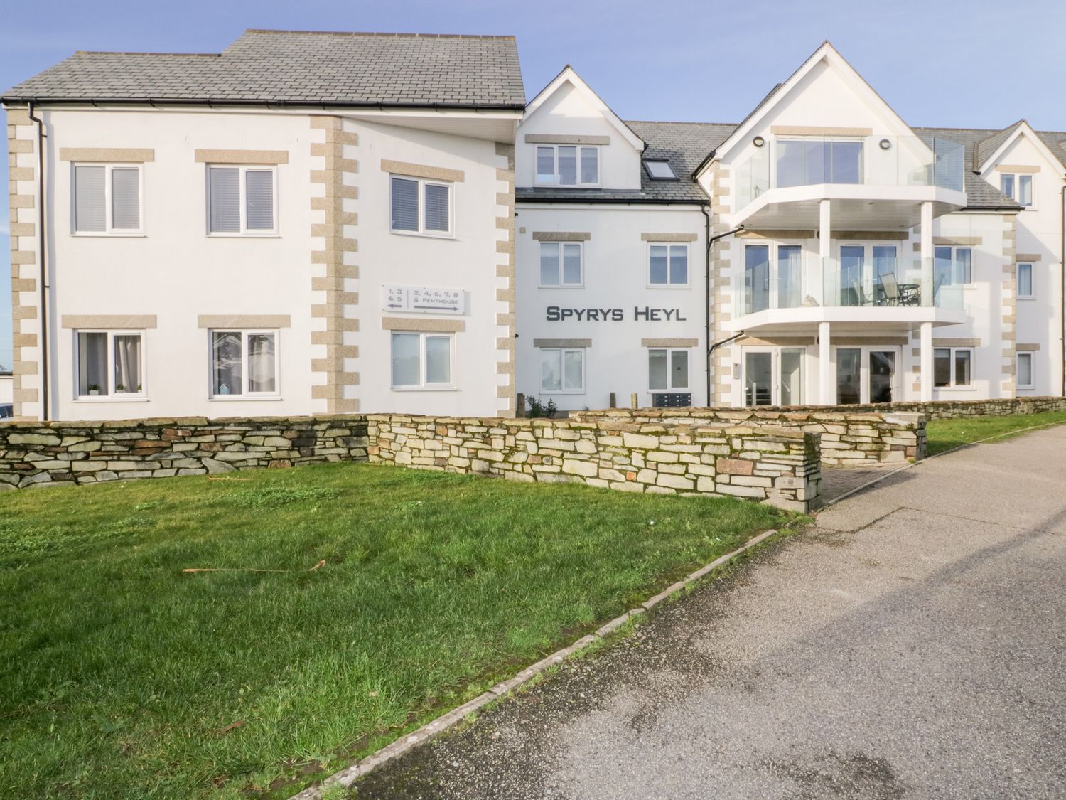 The exterior of a white residential building with balconies and a stone wall in front at 3 Spyrys Heyl in Newquay