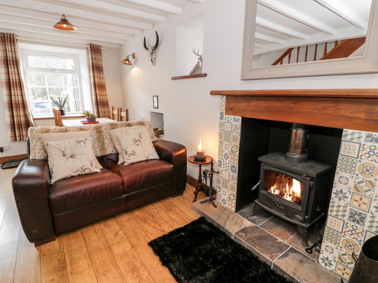 A living room with a brown leather sofa near a fireplace with a fire and patterned tiles at Encil in Beddgelert