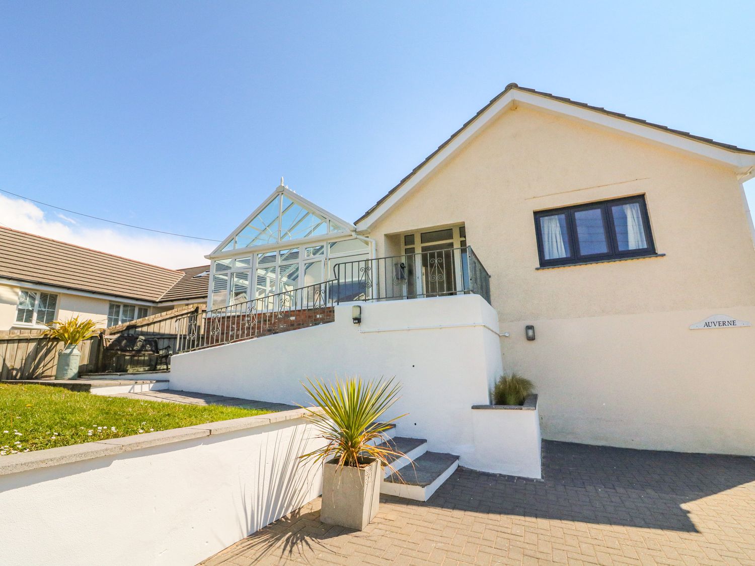 A white house with a glass conservatory and a small garden area at Auverne in Poundstock near Widemouth Bay