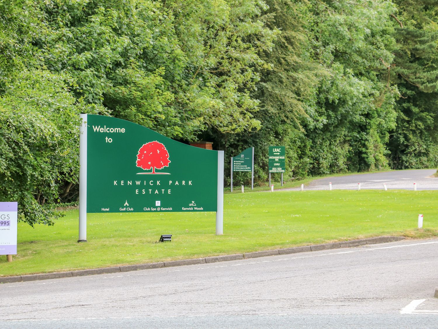 A green welcome sign for Kenwick Park Estate on grass beside a road with trees in the background at Great Leap in Louth