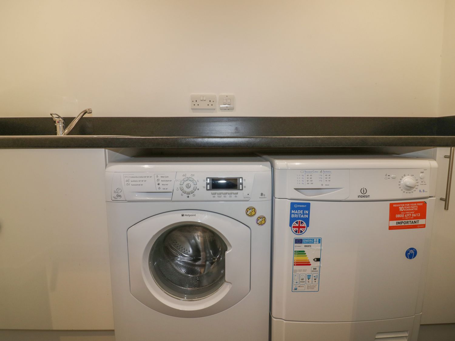 A laundry area with a washing machine and a dryer under a countertop with a sink at Stores & Supplies in Bodmin