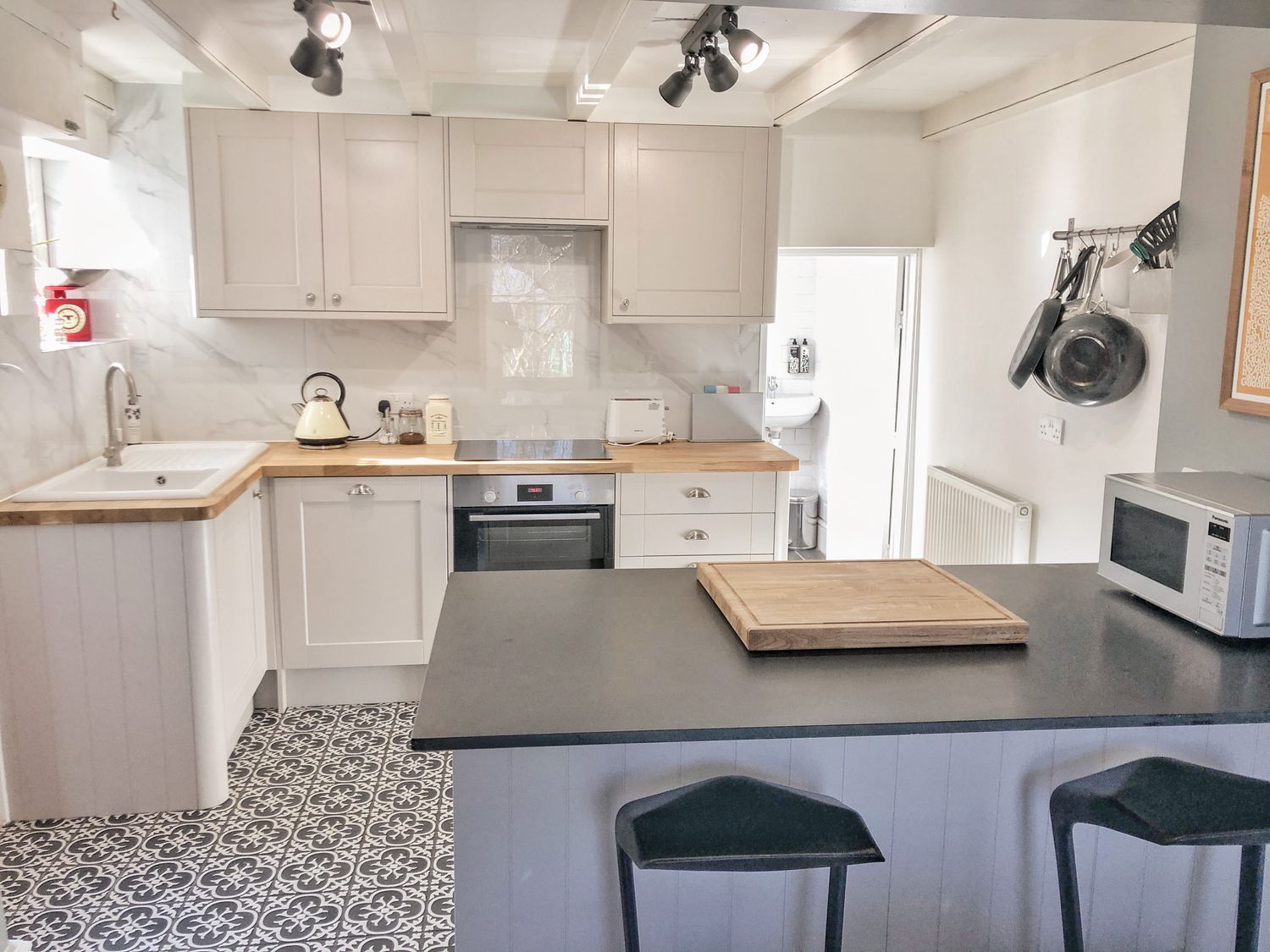 A kitchen with white cabinets black countertop wooden cutting board microwave and hanging pots at 21 British Road St Agnes
