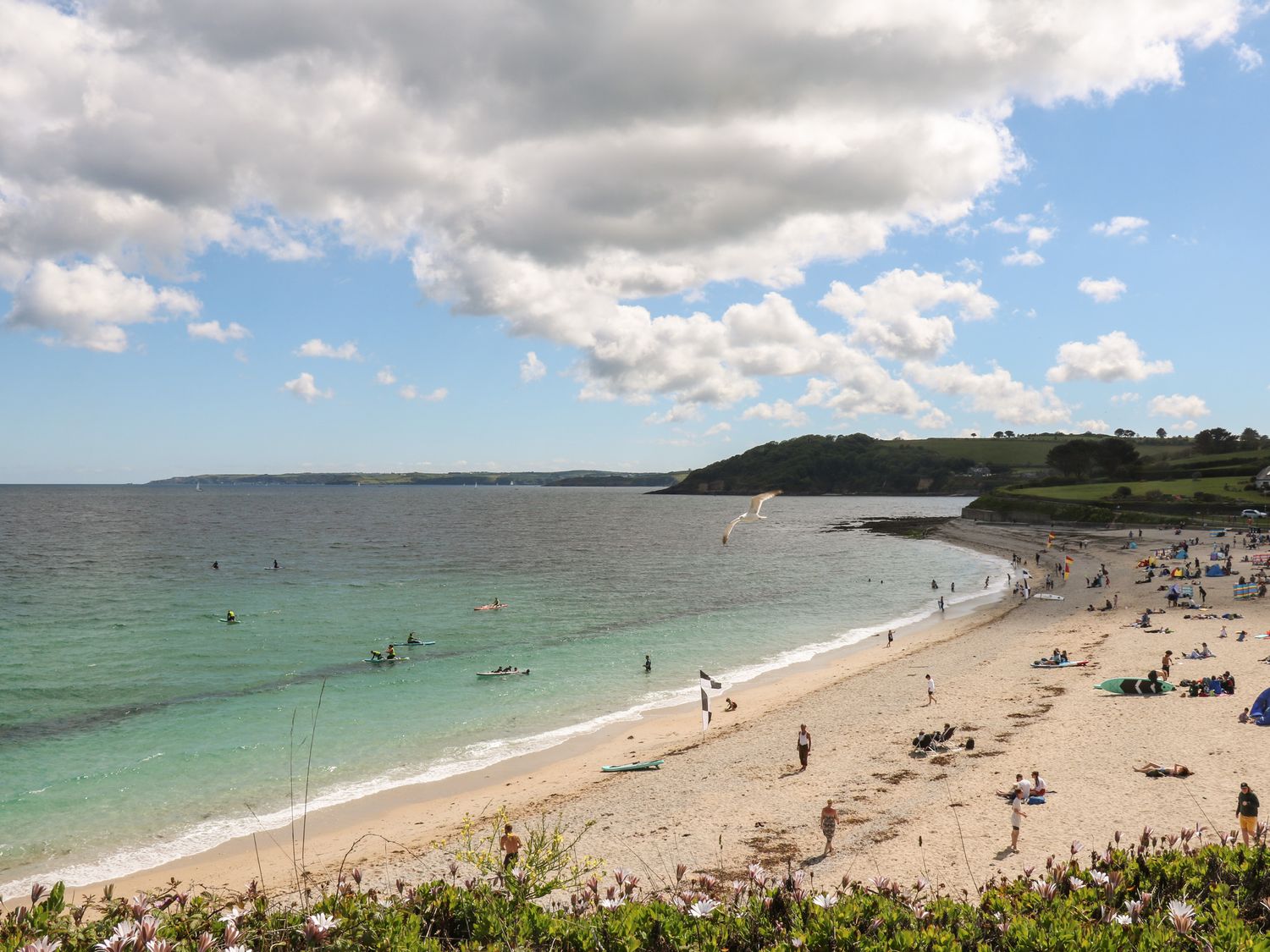A beach with people walking and swimming and green hills in the background at The Water House in Falmouth