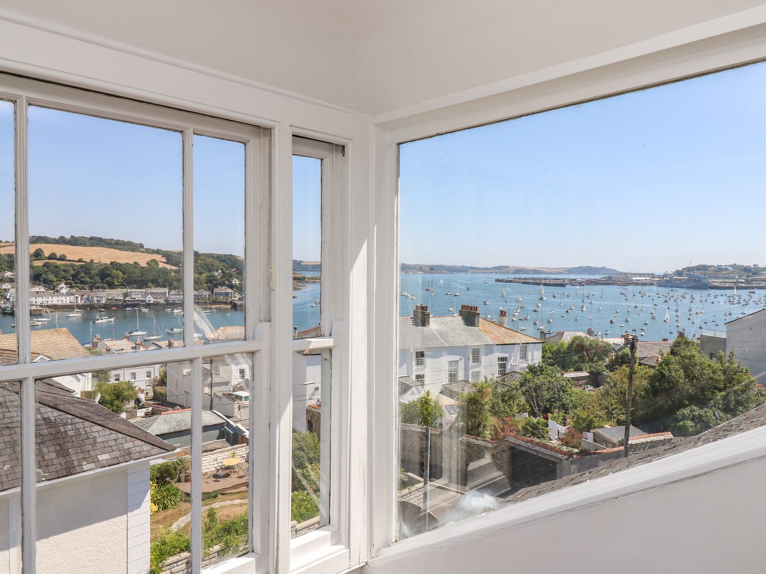 A view through corner windows showing houses, a harbor with many boats, and hills in the background at The Water House in Falmouth