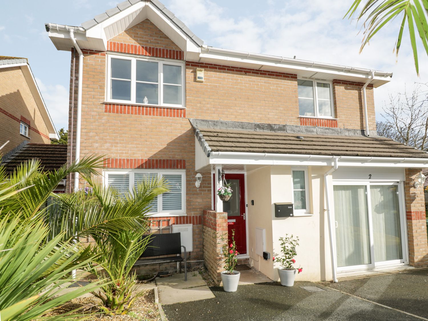 A two-story brick house with a red door and potted plants near the entrance at Two Bare Feet in Newquay