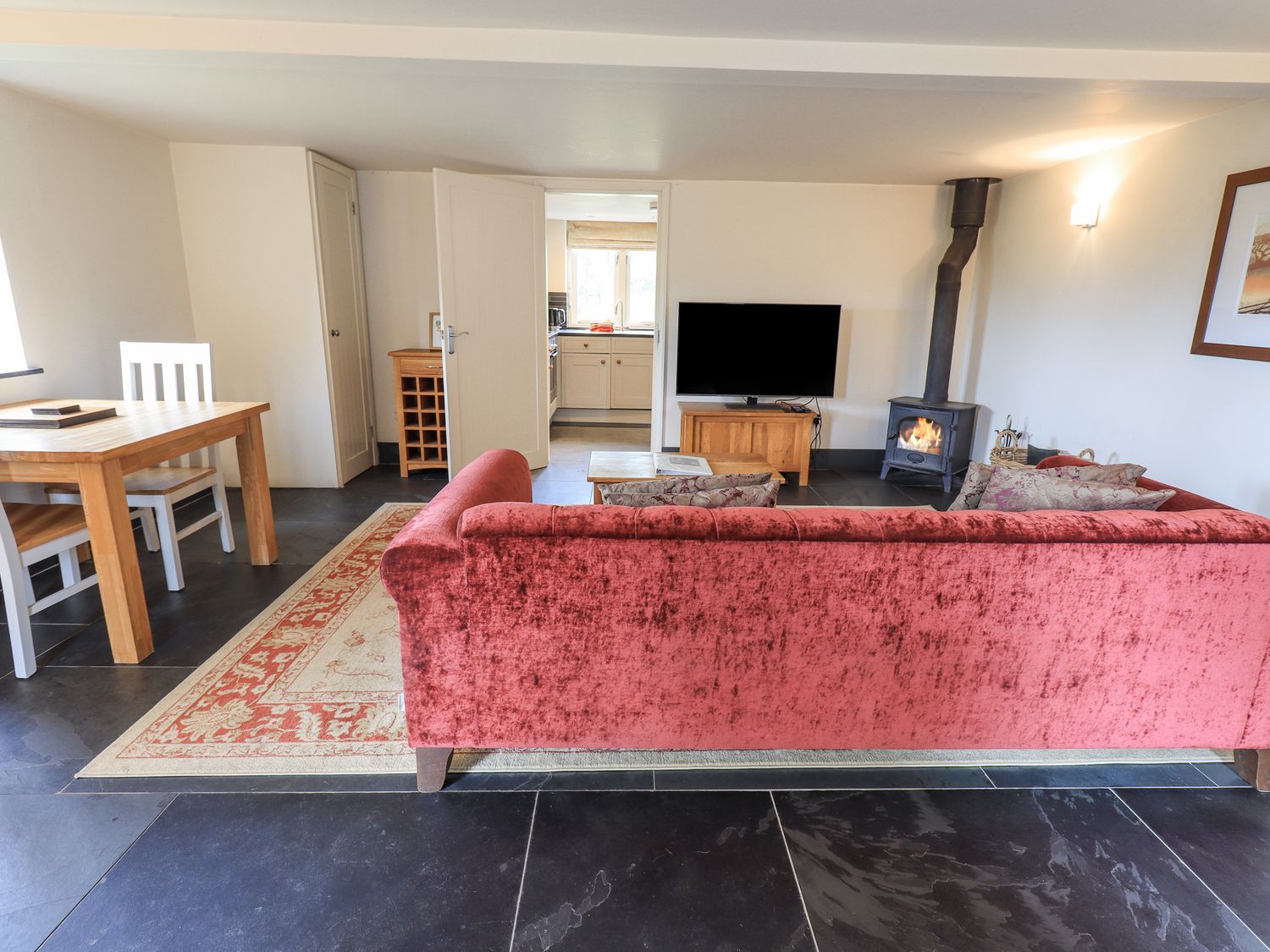 A living room with a red sofa a wood burning stove a television and a dining table at Dove Tail Barn in Kendal