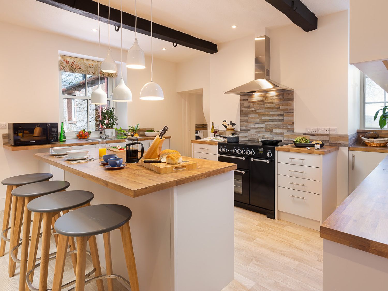 A kitchen with a wooden countertop island with stools and a black stove at Highgate in Hutton John near Ullswater