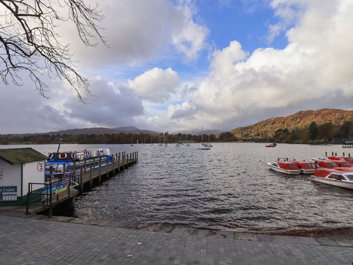 A lake with moored boats and a pier with a small building at Pure Grace in Ambleside