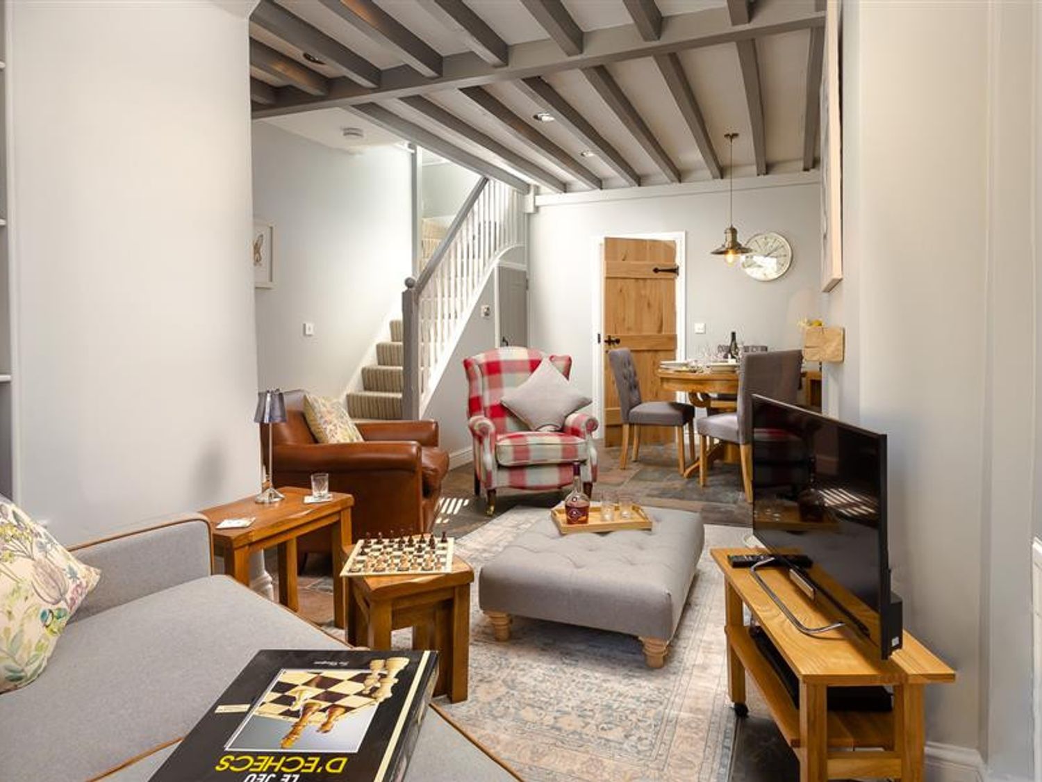 A living room with sofas, armchairs, a chess set, a television, a dining table with chairs, and a staircase at Little Leveret Cottage in Keswick