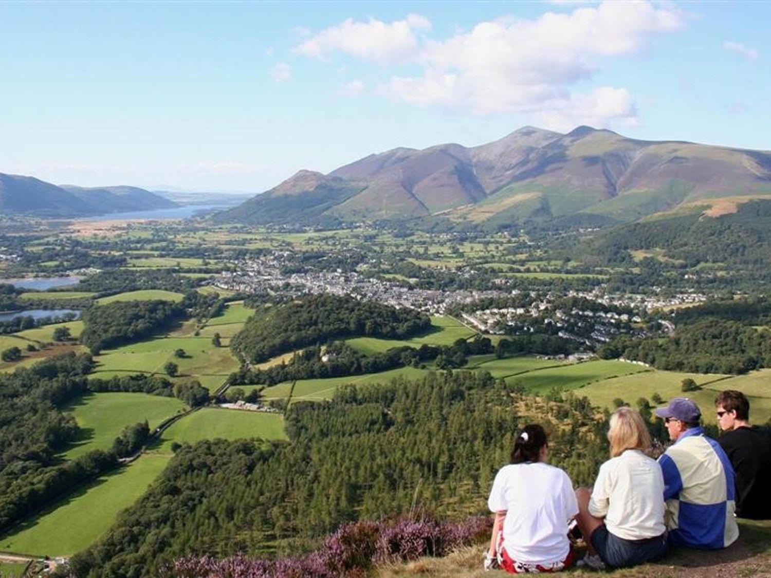 People sitting on a hill overlooking a valley with fields forests a town and mountains in the distance at Little Leveret Cottage in Keswick