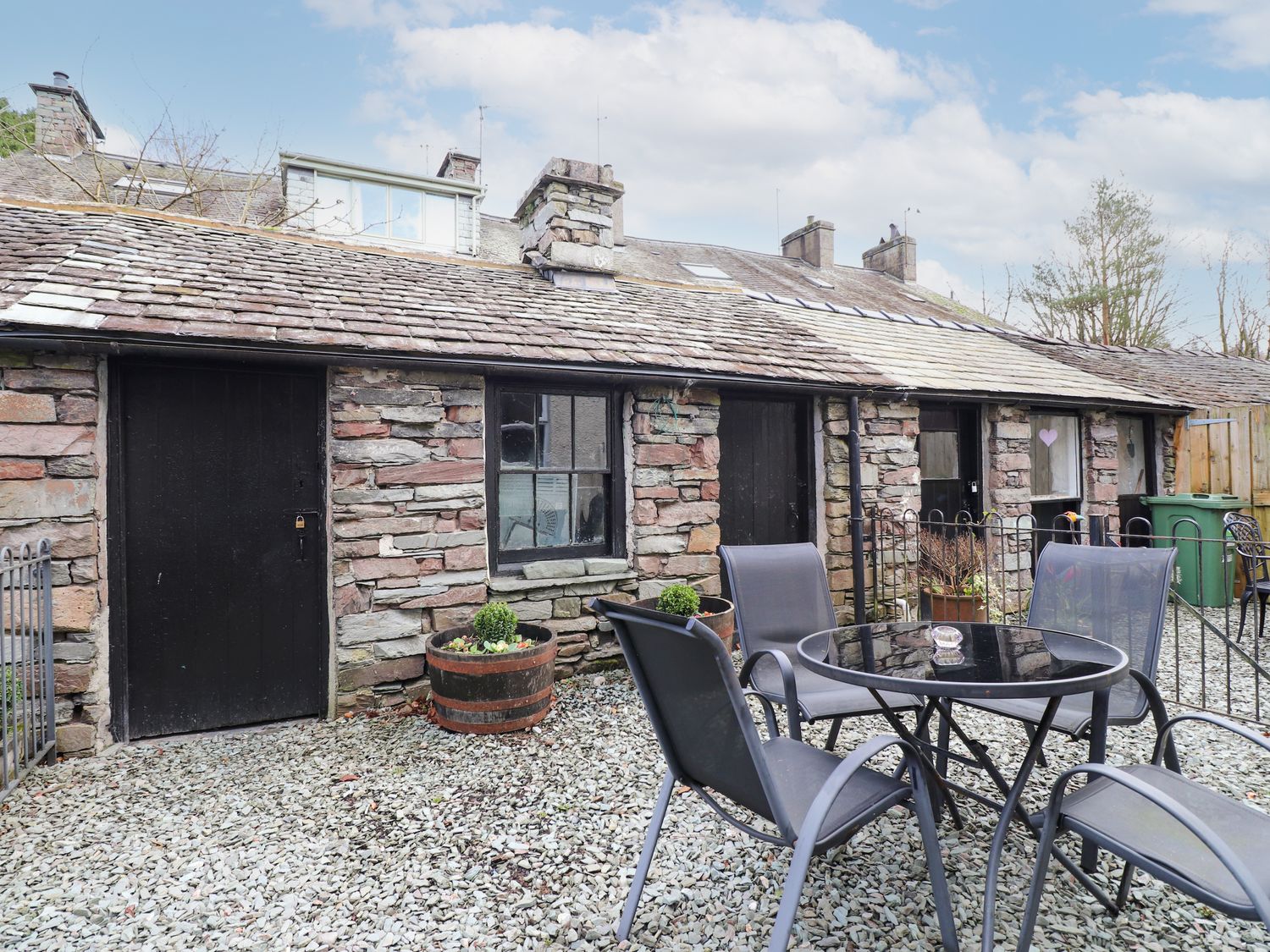 A stone cottage exterior with black doors and windows and outdoor seating at Becksteps Cottage in Grasmere
