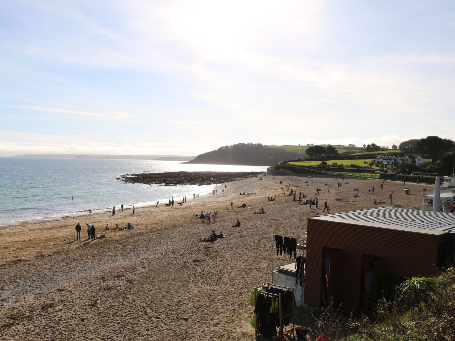 A sandy beach with people near the water and a small building with wetsuits hanging at Chycoose Hicks Mill near Perranarworthal