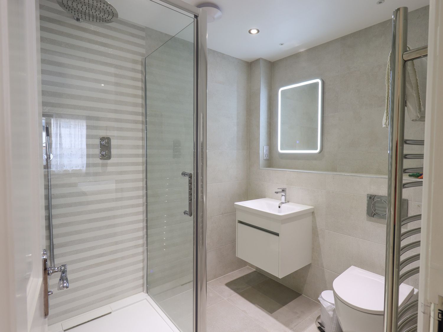 A bathroom with a glass shower enclosure a wall mounted sink a toilet and a lighted mirror at Romney 17 in Ambleside