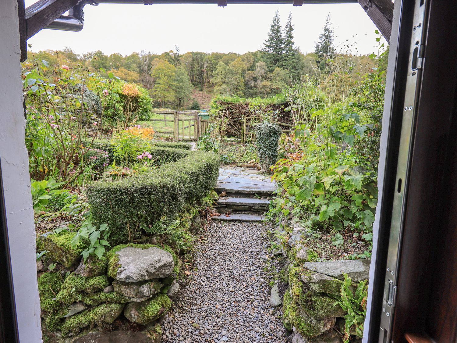 A garden with stone steps and a gravel path leading to a wooden gate at Park Cottage in Ambleside