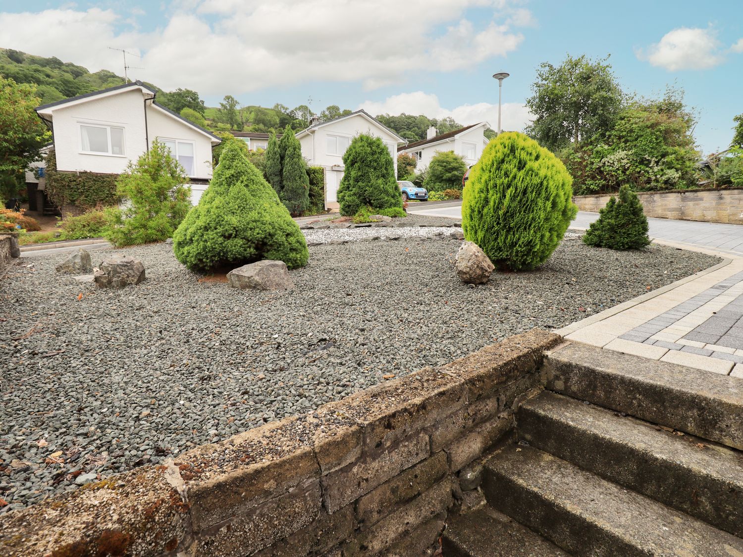 A front yard with gravel, conifer bushes, rocks, and steps leading to a paved driveway at Swirl How in Ambleside