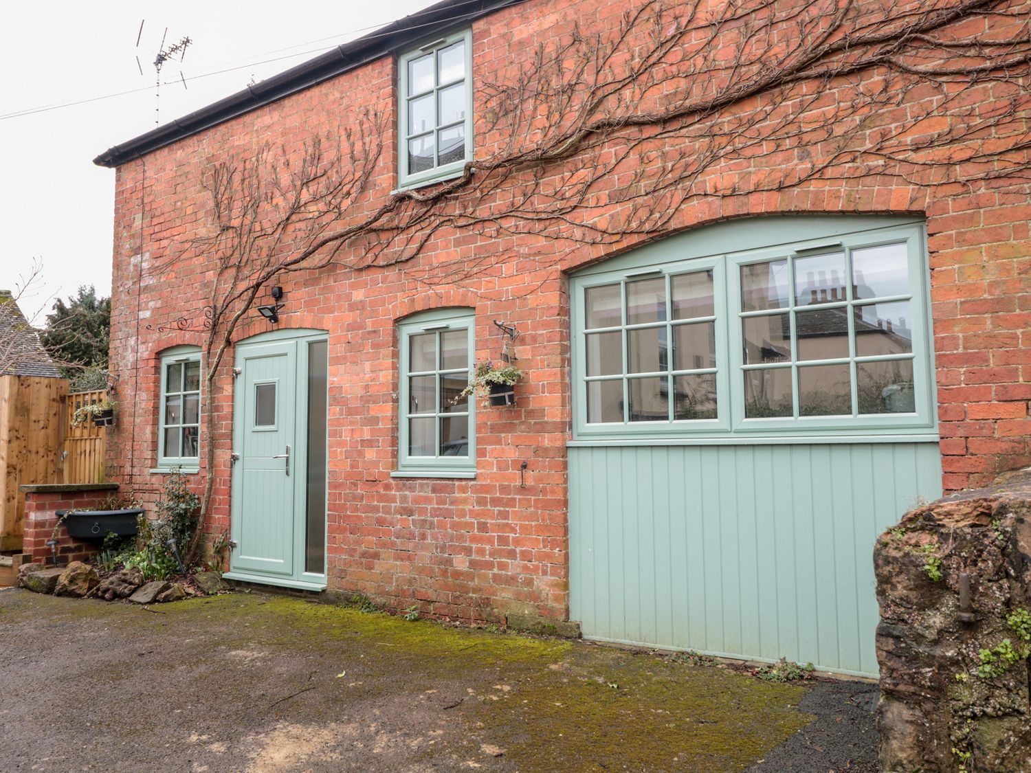 A brick house exterior with green framed windows and doors and climbing vines at Ostlers in Mitcheldean