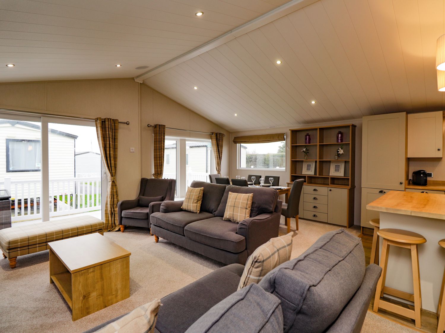 A living room with sofas, armchair, coffee table, and dining area with chairs and cabinet at 2 bedroom Lodge at Pevensey Bay in Pevensey Bay
