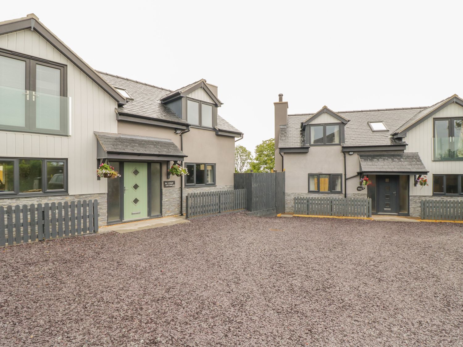 Two modern houses with fenced yards and gravel driveway at Big Azzles in Tyn-y-Gongl near Benllech