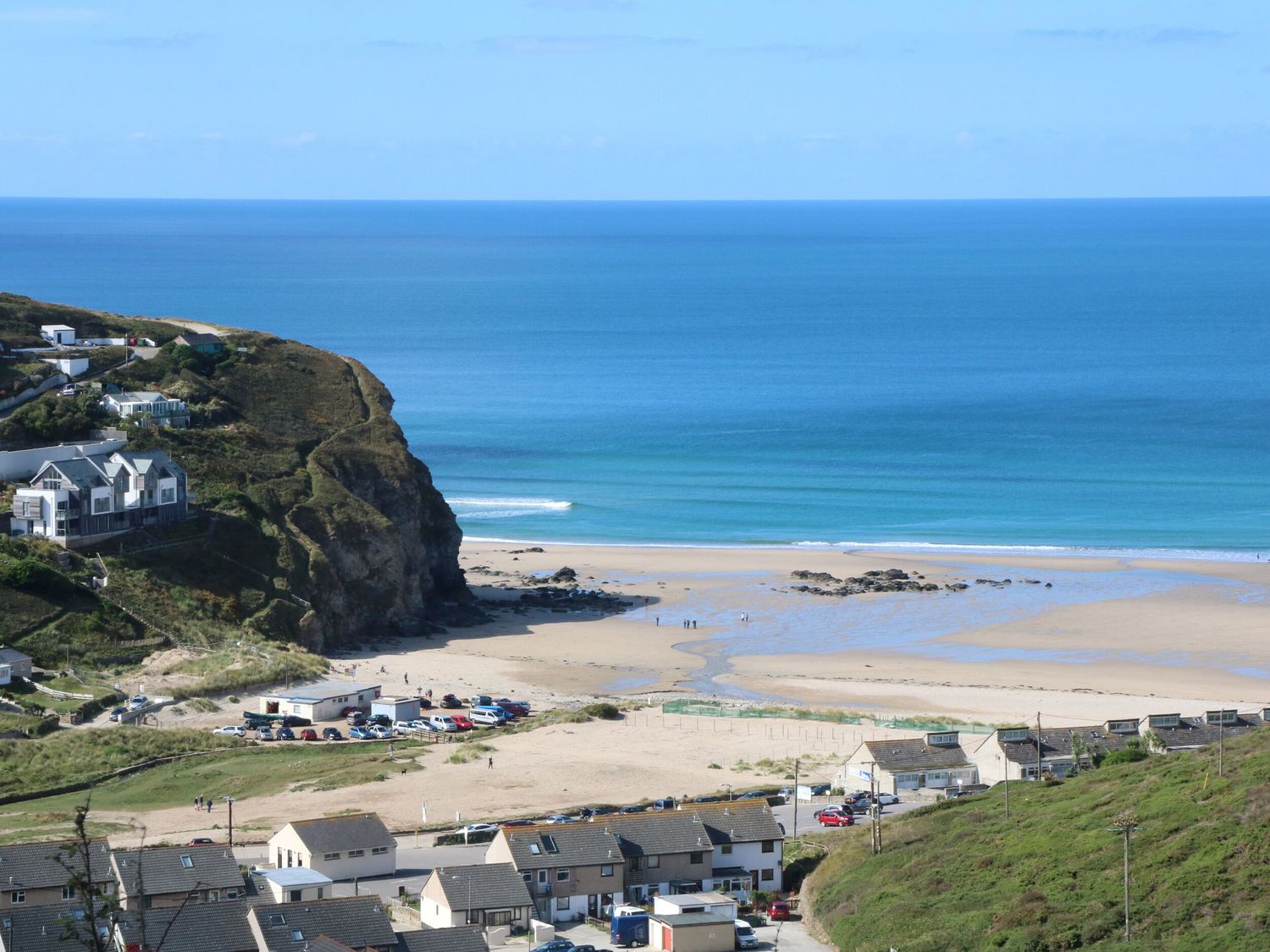 A coastal view of a beach with houses and parked cars near the shore at Gecko Beach in Porthtowan