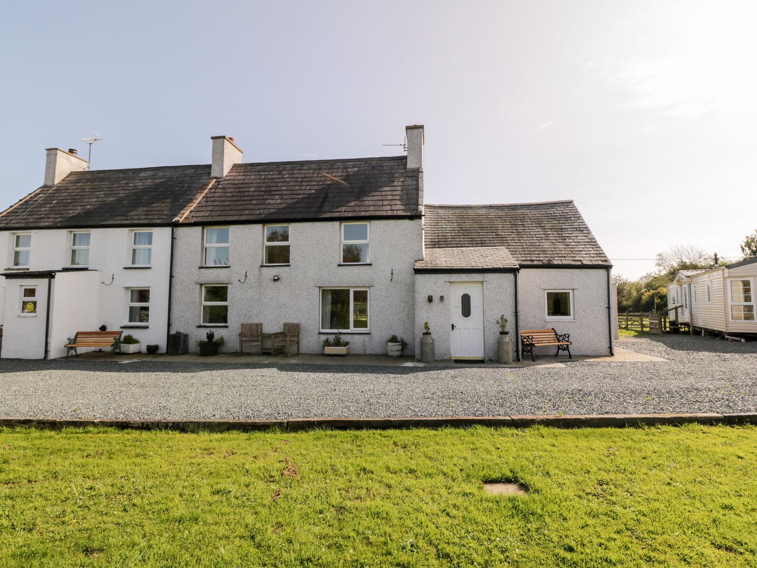 A row of white houses with slate roofs and benches outside on a gravel area at Penllyn in Newborough