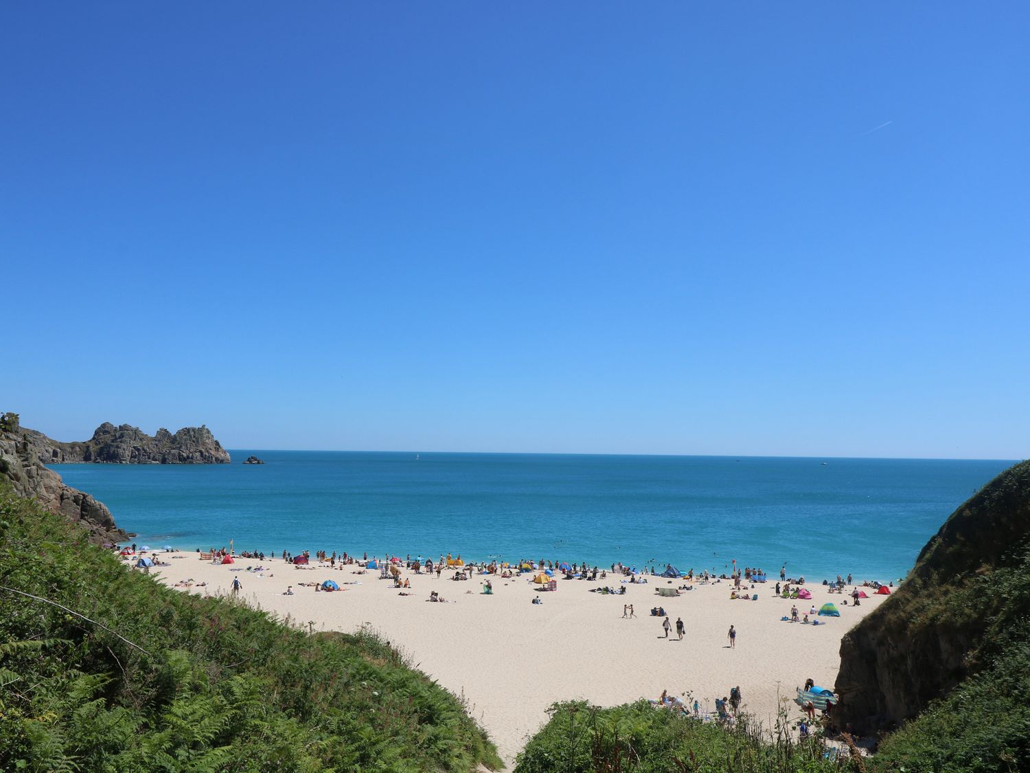 A sandy beach with people and umbrellas near the ocean and rocky cliffs at Longships in Porthcurno