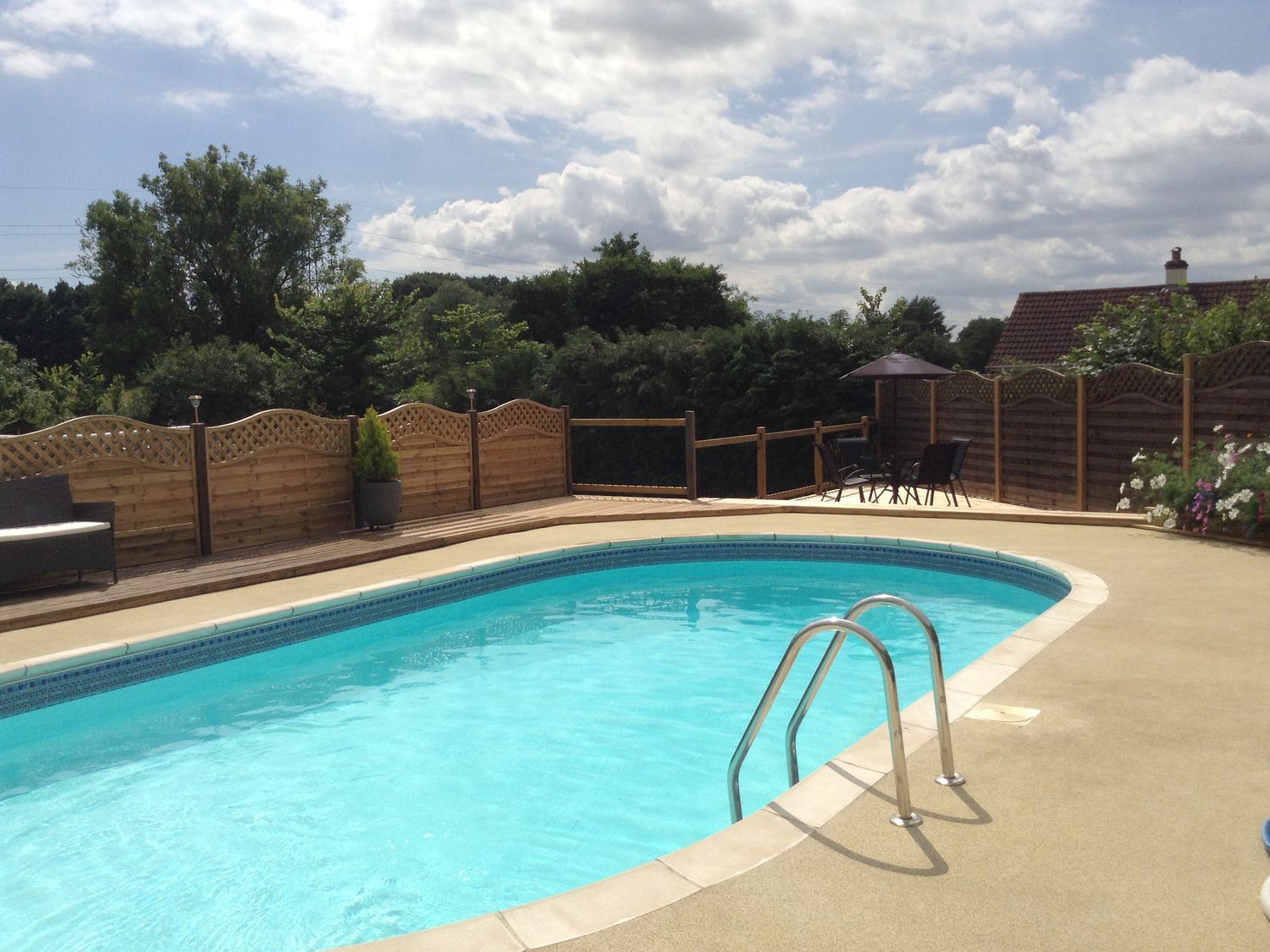 An outdoor swimming pool with a metal ladder surrounded by a wooden fence and trees at Broadclyst Cottage in Ottery St Mary