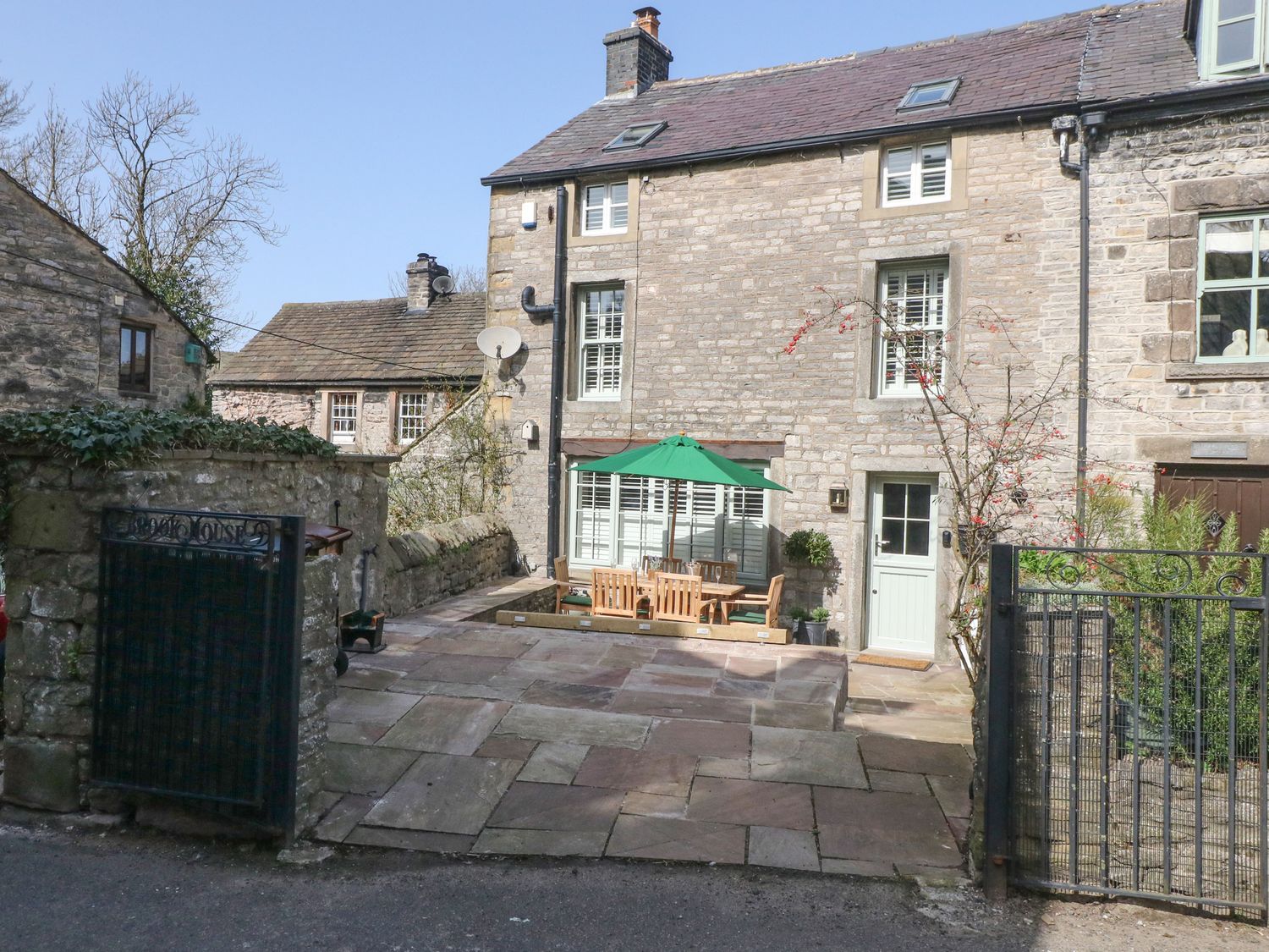 Stone cottage with enclosed patio area and outdoor dining table with green umbrella at Brookhouse in Castleton Peak District