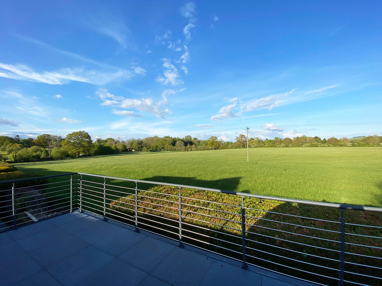 A balcony overlooking a large green field with trees and a blue sky at Vale Lodge in Pewsey