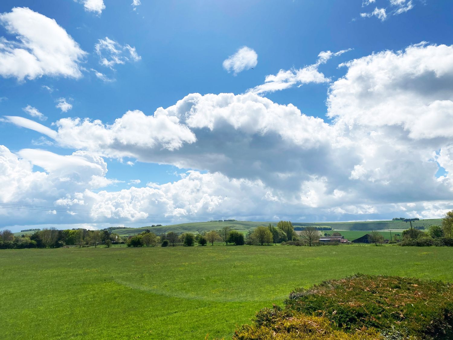 A green field with trees and buildings under a blue sky with clouds at Vale Lodge in Pewsey