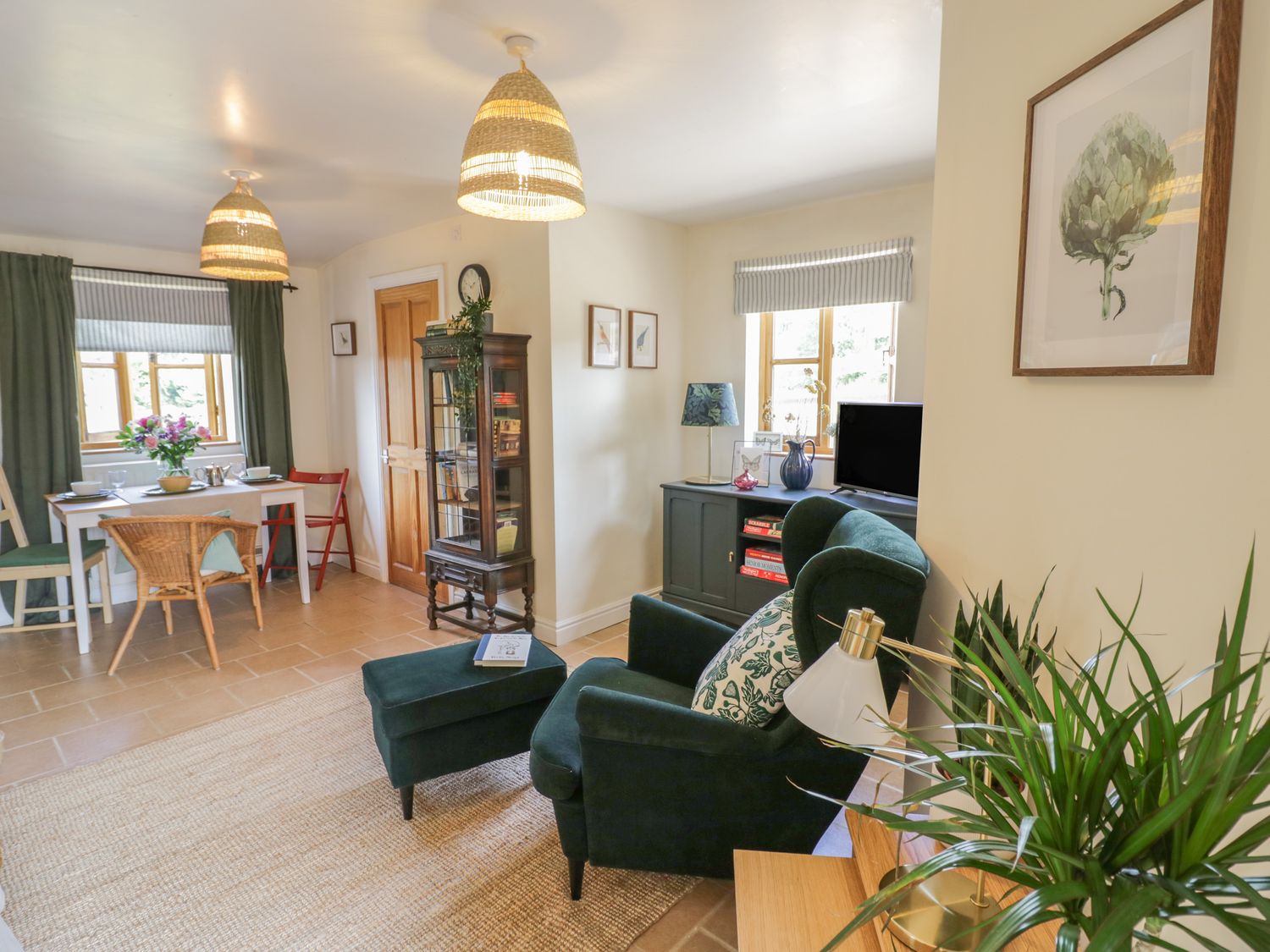 A living area with a green armchair and ottoman near a black cabinet with a television and a dining table with chairs and flowers at Holmer Farm Pudleston near Leominster