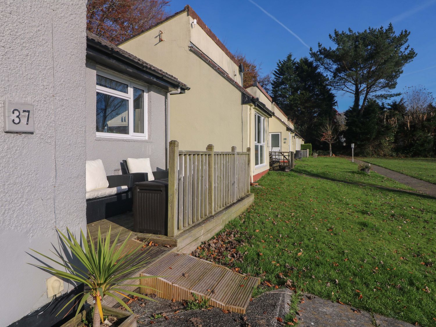 Exterior view of a row of single-story houses with small wooden decks and green lawn at Little Jack's in Callington