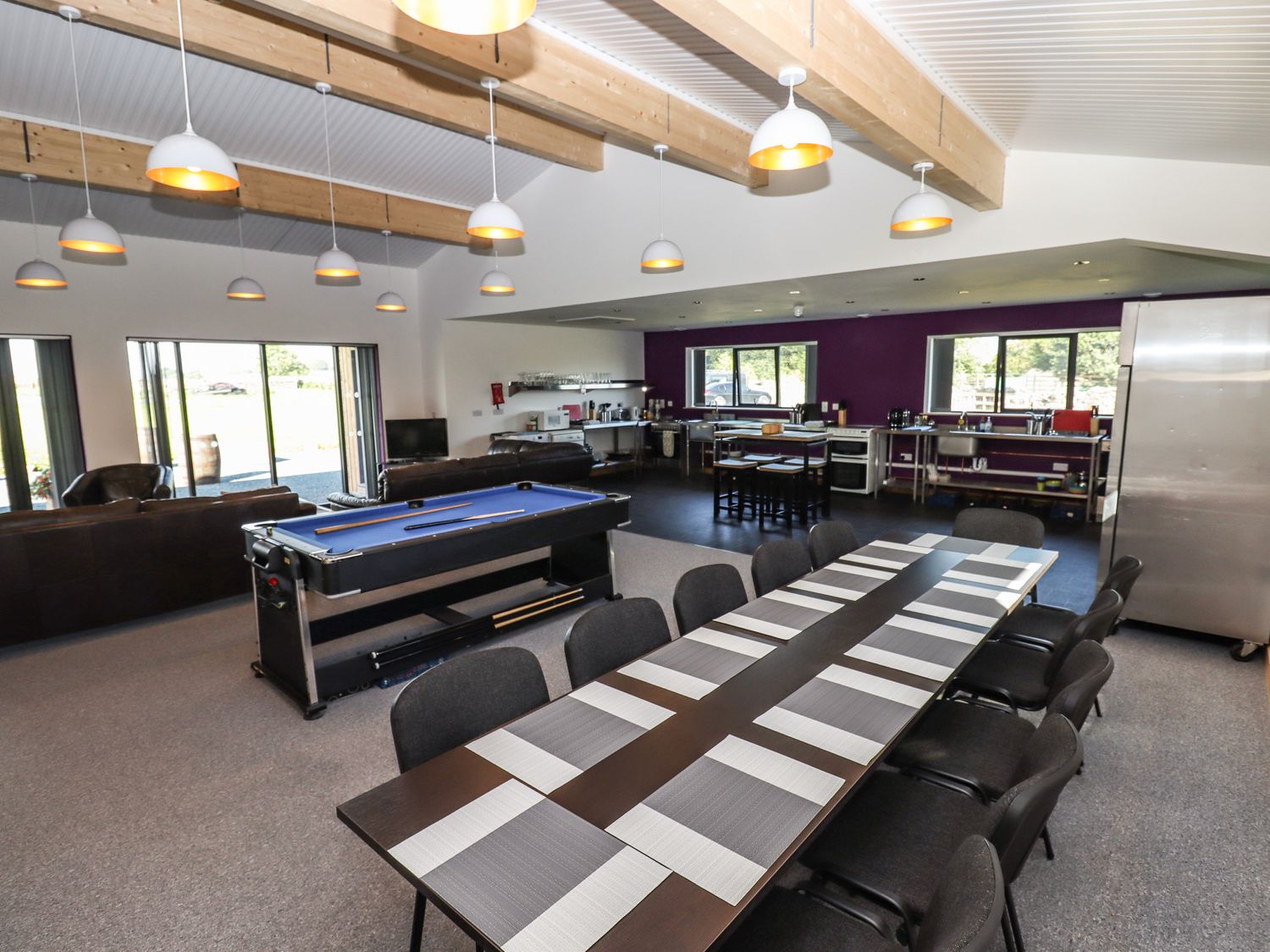 A large room with a long dining table with chairs a pool table couches and an open kitchen at Dales Lodge in Ingleton
