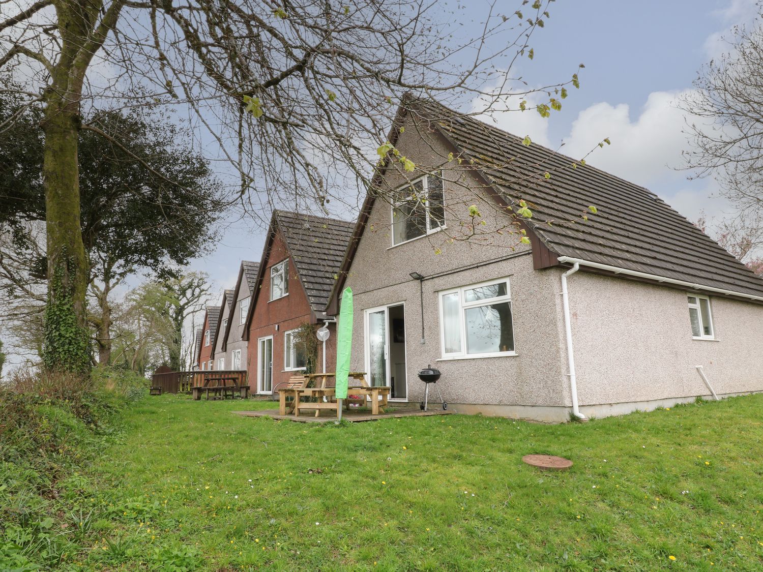 A row of similar detached houses with pitched roofs and picnic tables on grassy lawns at Hembry Meadows in Honicombe Park near Gunnislake