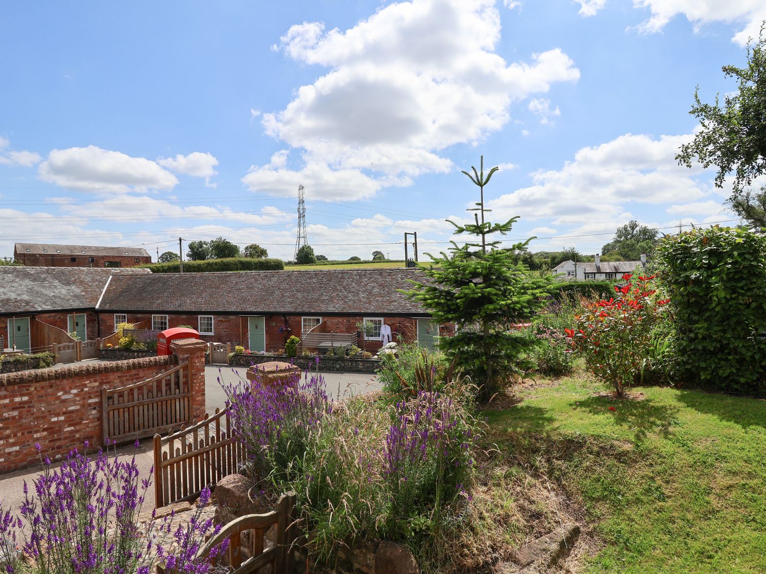 A garden with flowers trees and wooden gates in front of a row of brick buildings at The Hay Barn in Chester