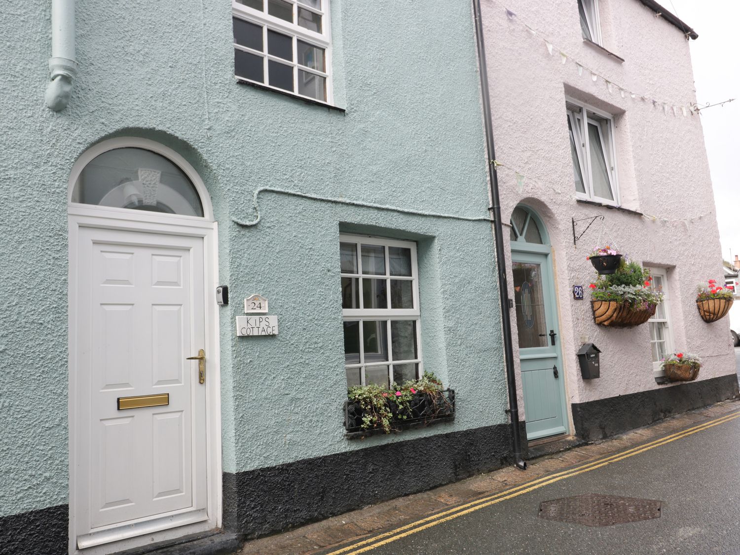 The exterior of cottages with white and light blue doors and windows with flower baskets on the walls at Kips Cottage in Mevagissey