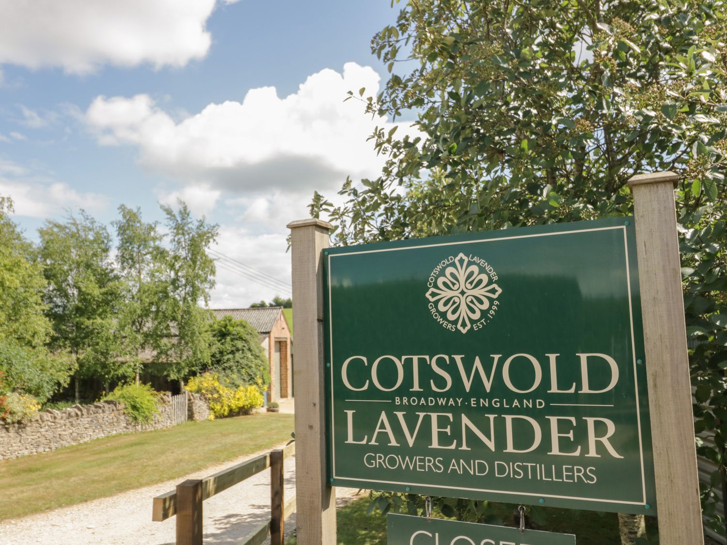 A green sign for Cotswold Lavender growers and distillers near a tree and pathway at Molly's Bit in Church Westcote near Bourton-On-The-Water