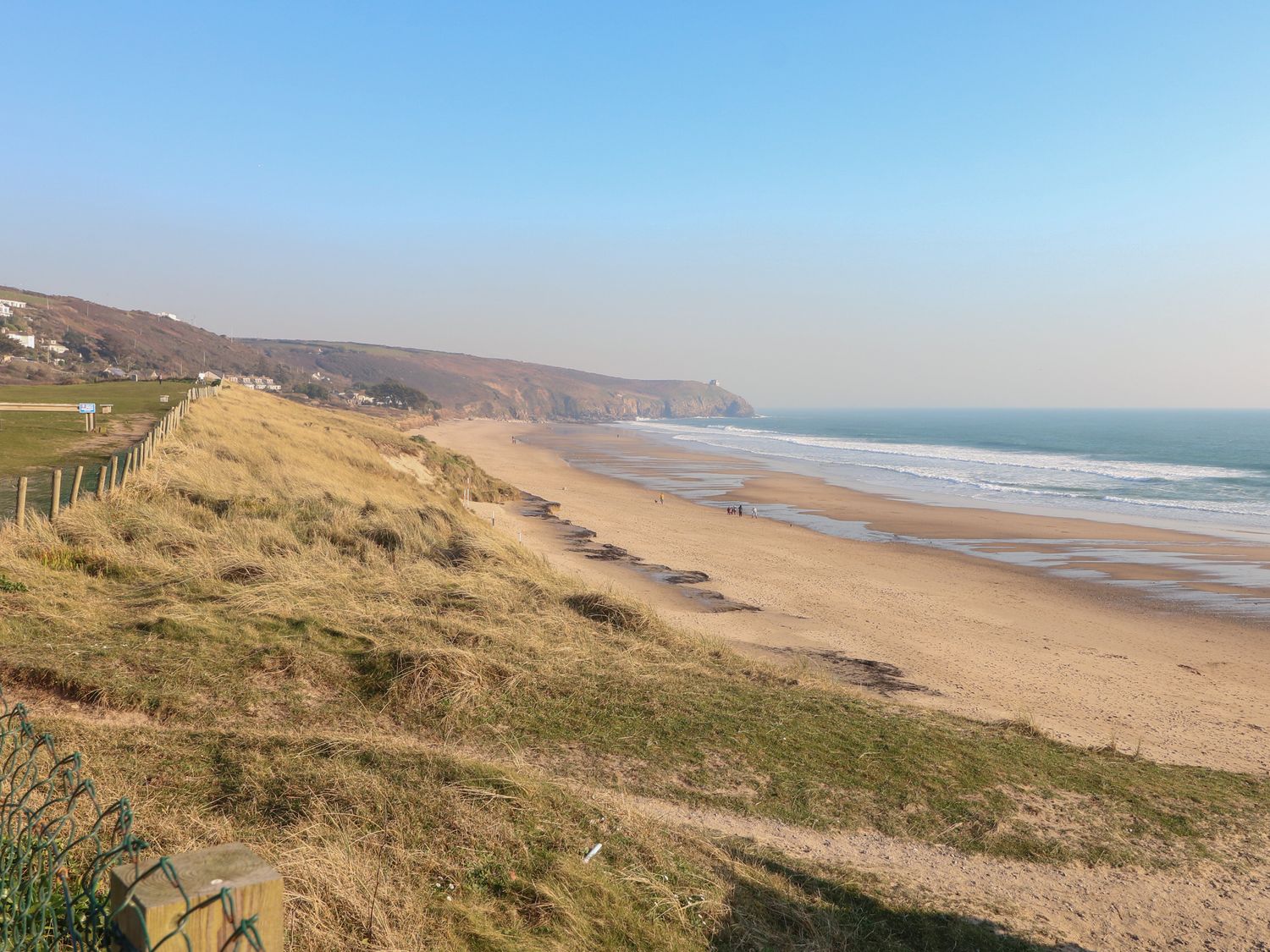 A sandy beach with waves and grassy dunes along the coastline at Sea Sands in Praa Sands