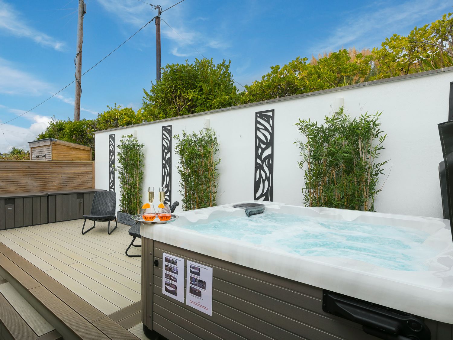 An outdoor patio with a hot tub champagne glasses two chairs plants and decorative wall panels at Sea Sands in Praa Sands