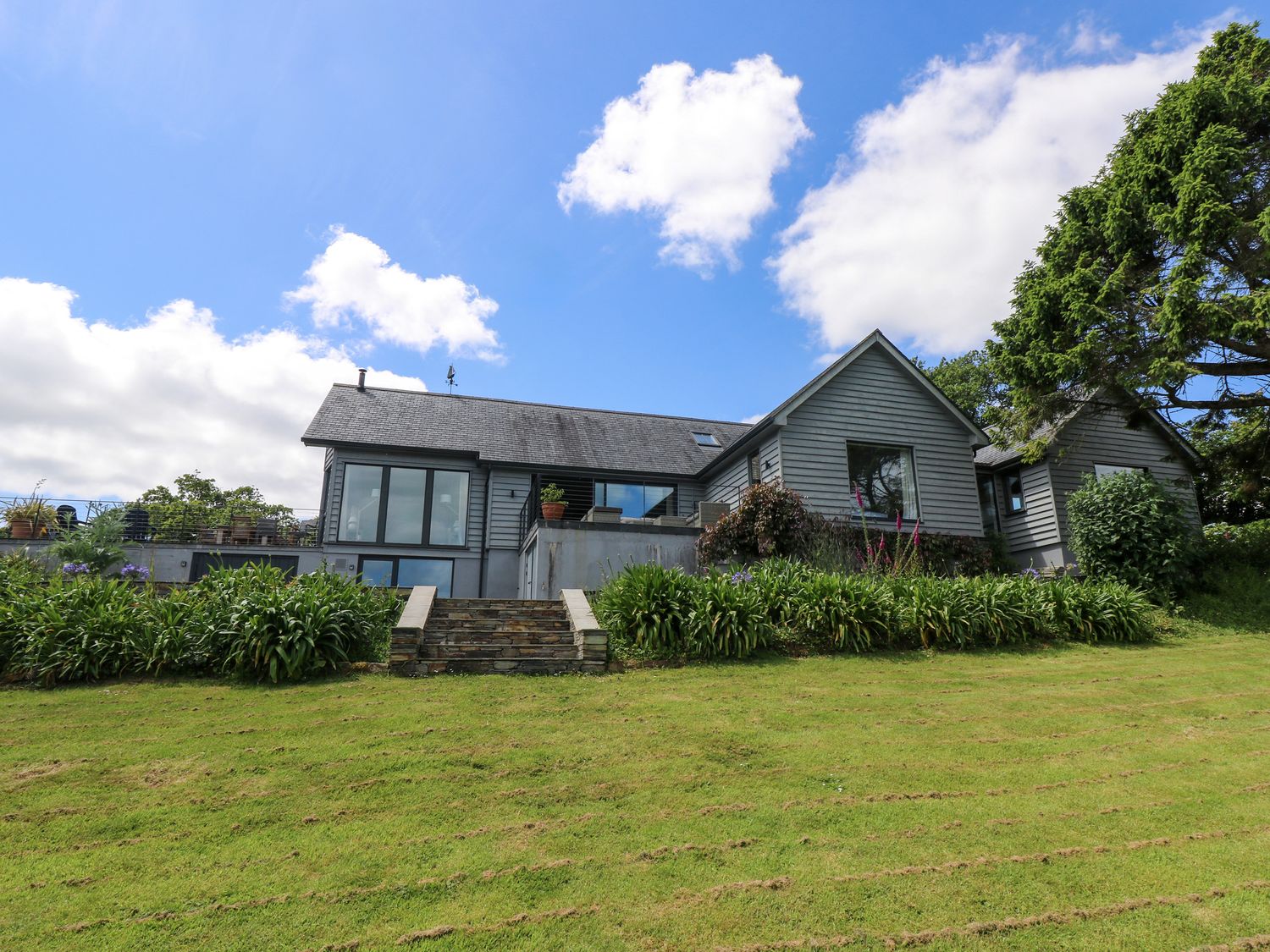 A house with large windows surrounded by plants and a lawn at Wood Meadow in Helford