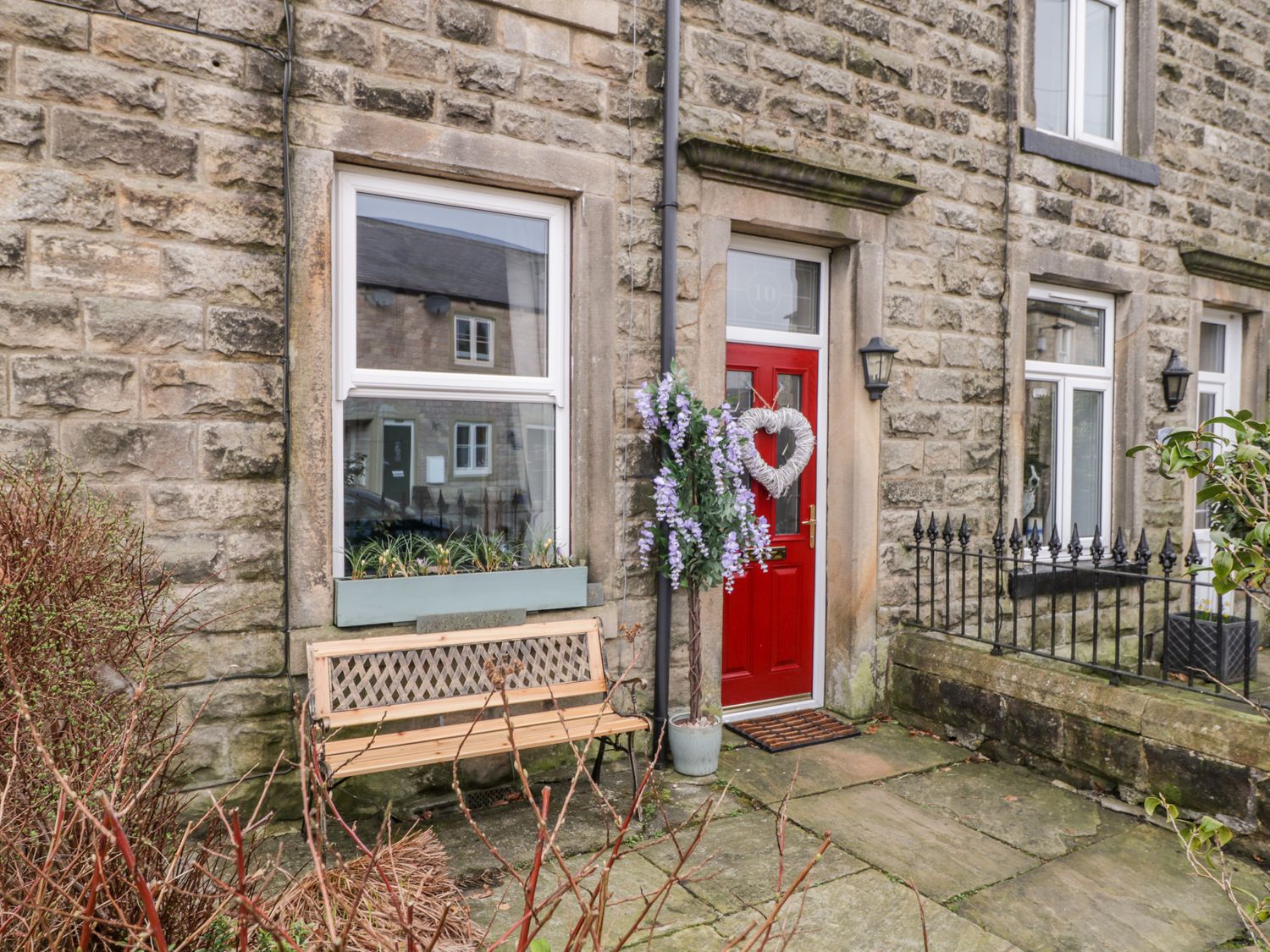 A stone exterior of a house with a red door a bench and potted plant at Crag View Cottage in Embsay