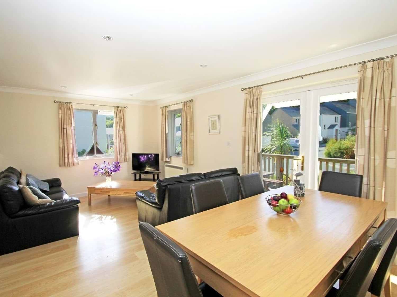 A living room and dining area with black leather sofas a wooden dining table with black chairs and a bowl of fruit at Waters Edge in Falmouth
