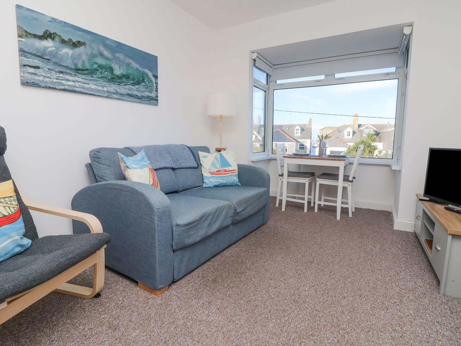 A seating area with a blue sofa and armchair with a dining table and chairs by a large window at The Beach Hut in St Ives