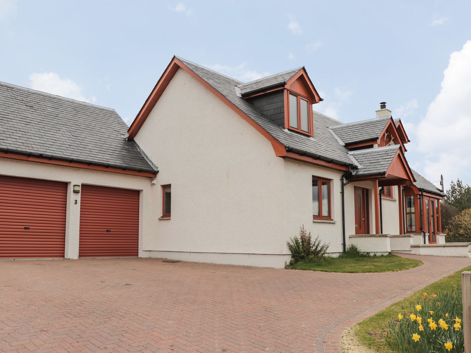 The exterior of a house with a double garage with red doors and a driveway at 3 Croftside in Aviemore