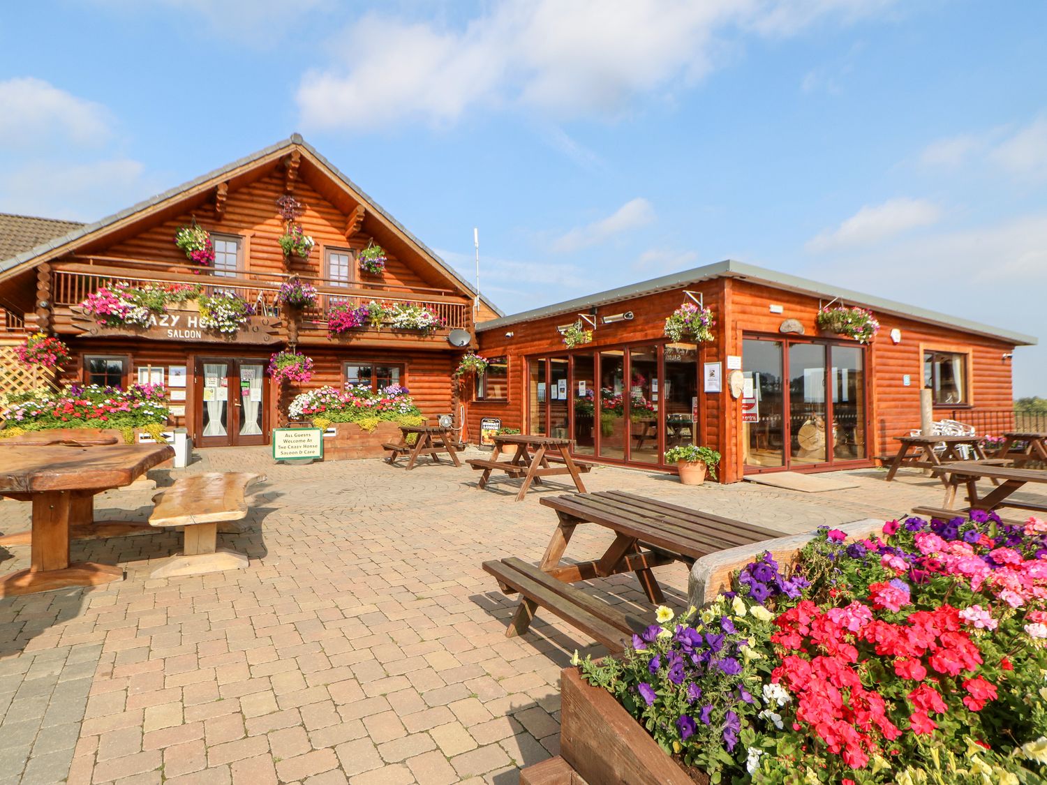 An outdoor seating area with wooden picnic tables and flower planters outside a log cabin building at Jalan End in Felton
