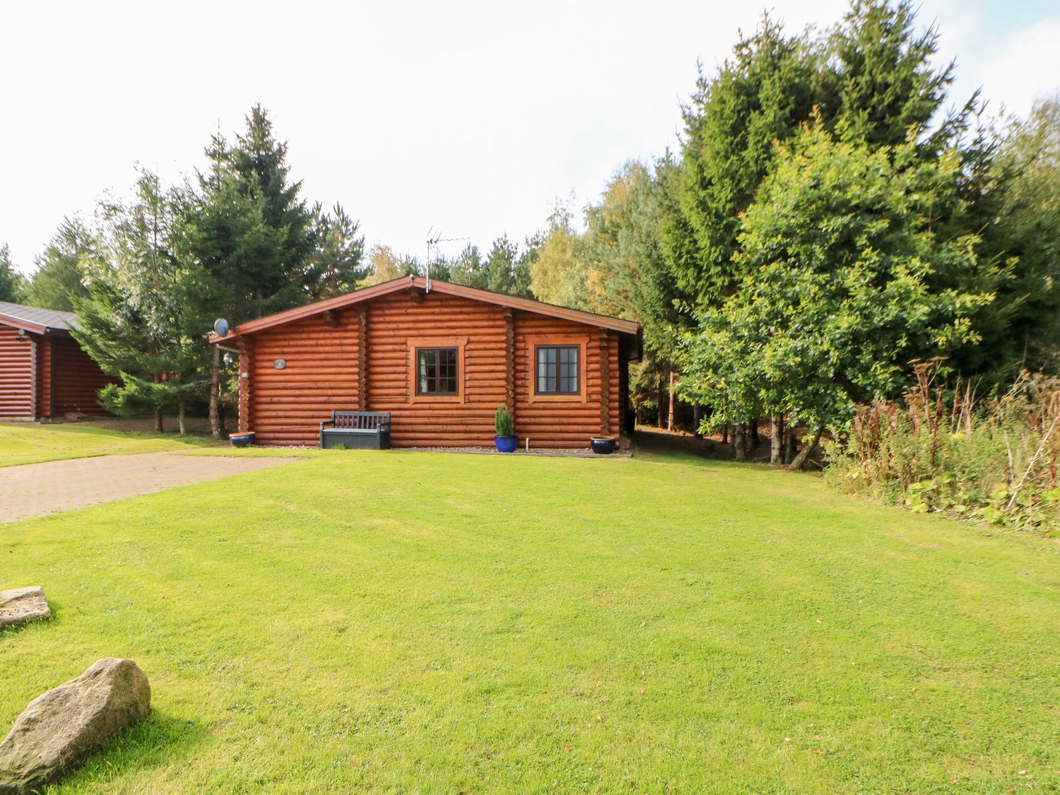 A log cabin with two windows a bench and potted plants on a grassy lawn surrounded by trees at Jalan End in Felton