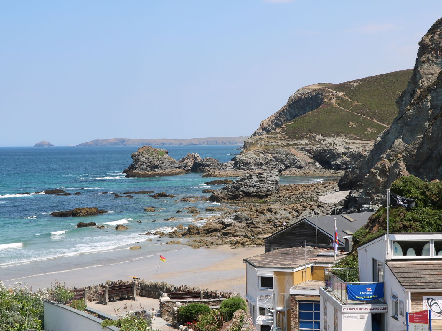A rocky coastline with a sandy beach and buildings near the shore at Alice Cottage Wheal Kitty near St Agnes