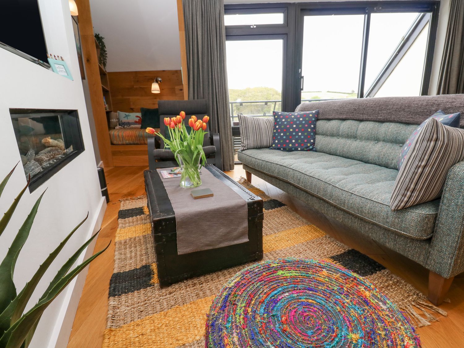 A living room with a green sofa with cushions and a coffee table with flowers at The Crows Nest in Maenporth near Falmouth Cornwall