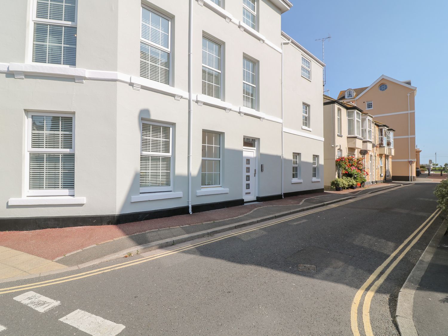 A street view with white buildings and windows with blinds and plants on the sidewalk at Sea Aster in Teignmouth