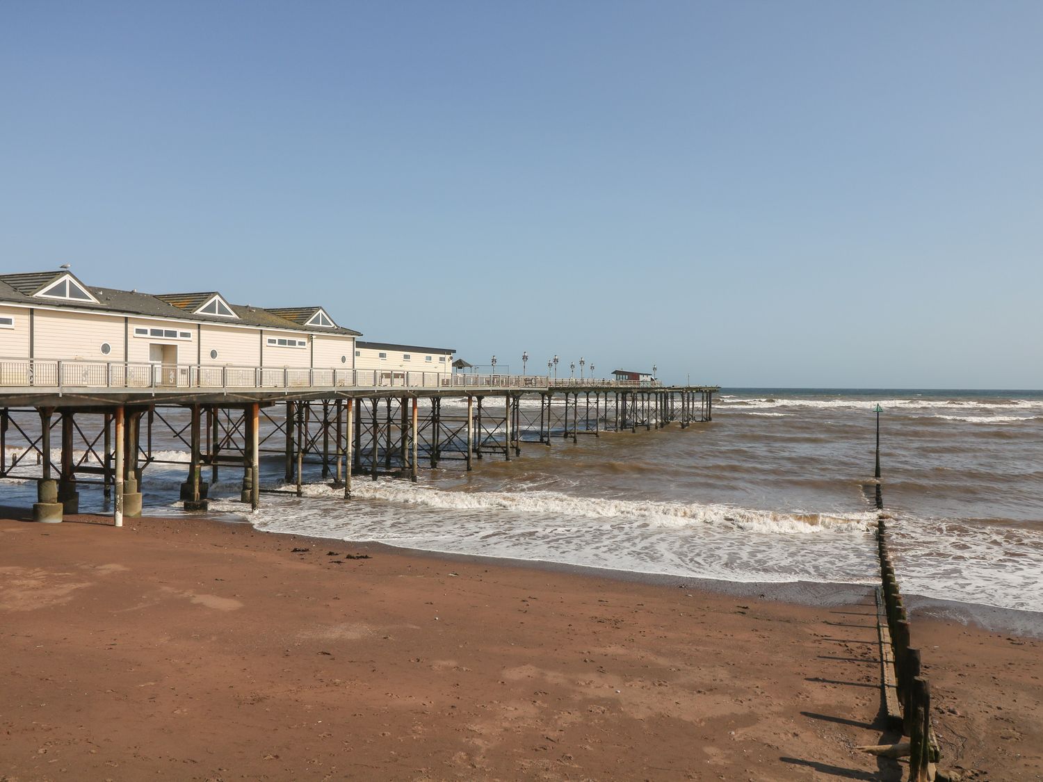 A wooden pier extending over the sea with a sandy beach in the foreground at Sea Aster in Teignmouth
